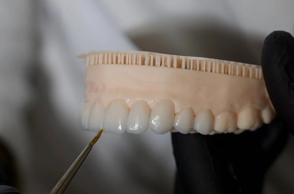 A full porcelain arch held in a gloved hand while it is characterized with a fine brush.
